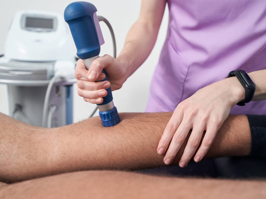 Physiotherapist using a shockwave therapy device on a patient alongside physical rehabilitation exercises at Apex Physio.