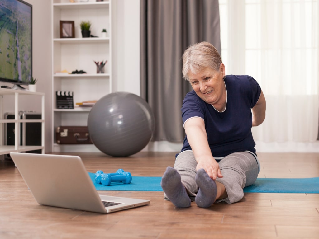 An older woman participating in a telehealth virtual physiotherapy session at home using a laptop.