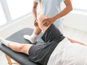 A physiotherapist performing manual knee assessment and joint rehabilitation during a physical therapy session.