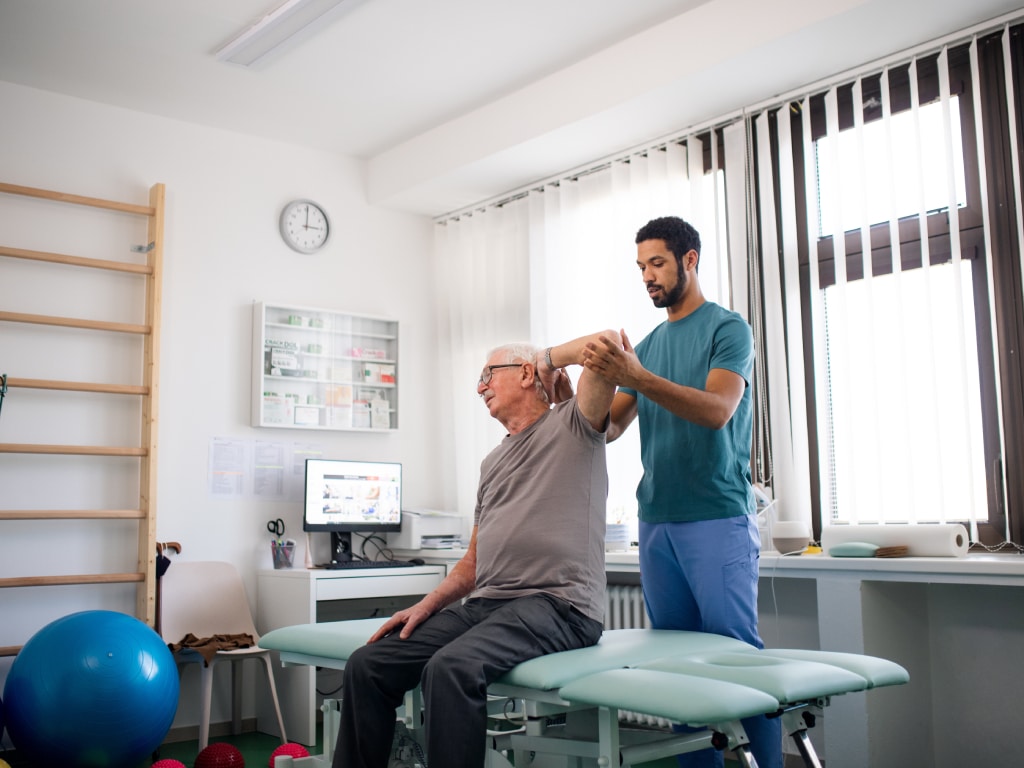 A physiotherapist performing shoulder range-of-motion therapy on an older patient at a rehabilitation clinic.