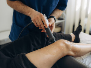 Physiotherapist administering shockwave therapy treatment to a patient's knee joint in a Pickering clinic.