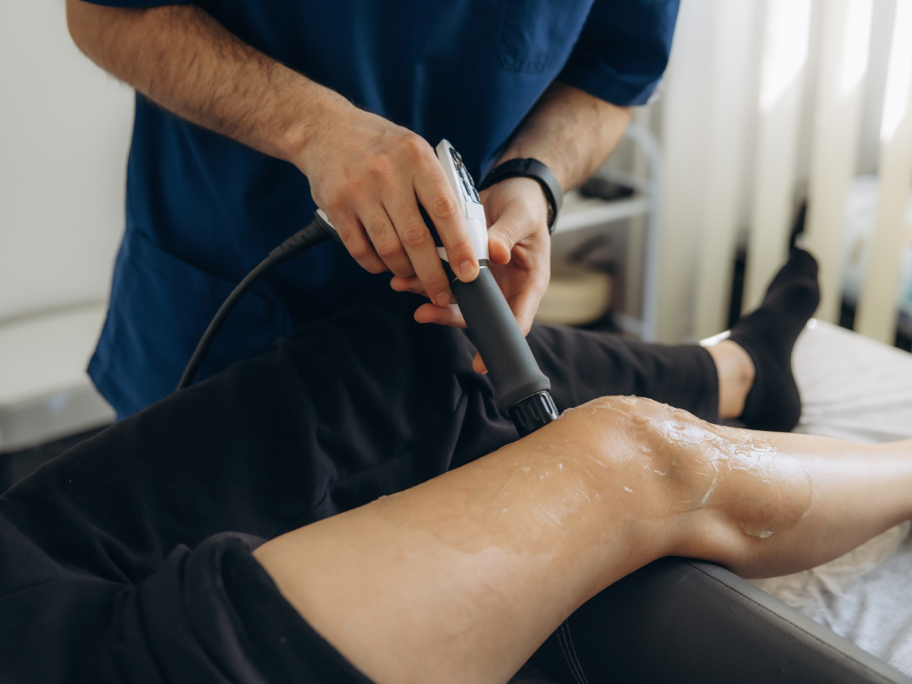 Physiotherapist administering shockwave therapy treatment to a patient's knee joint in a Pickering clinic.